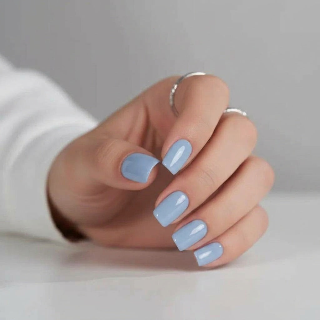 Baby Blue press-on naglar i ljusblå fyrkantig form mot vit bakgrund, hand med tunna silverringar