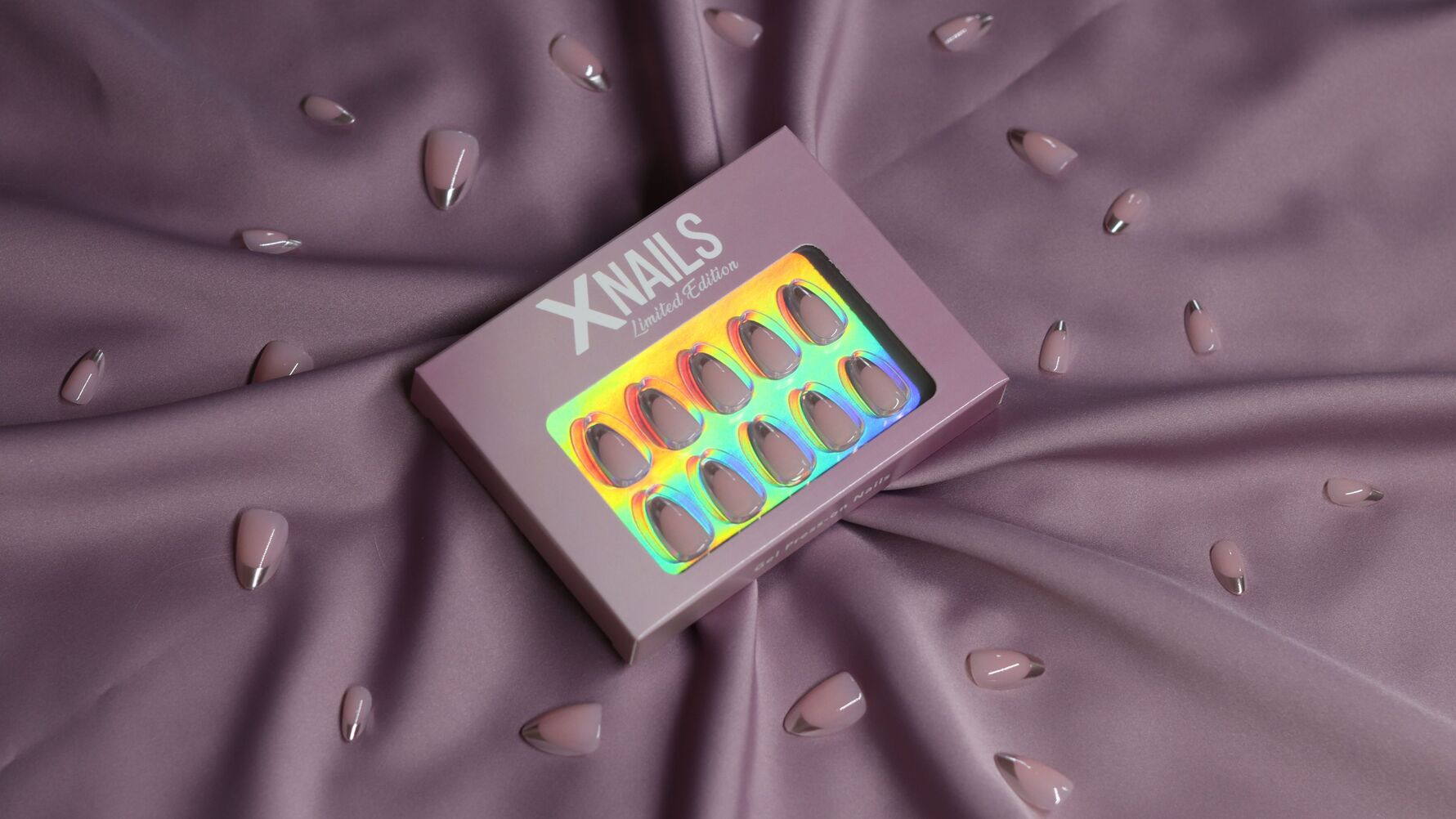 Limited Edition XNails Press-on-Nägel, hellrosa mandelförmig mit Chromspitzen, in und neben Verpackung auf lila Stoff