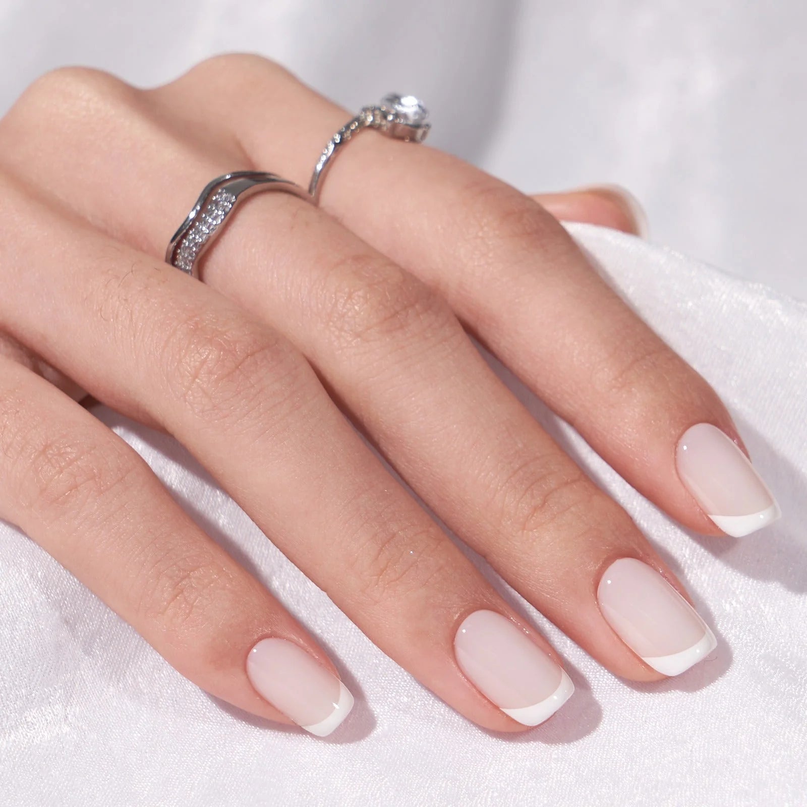 Frosted French gelénegle nærbillede square fransk manicure med sølvringe mod hvidt stof