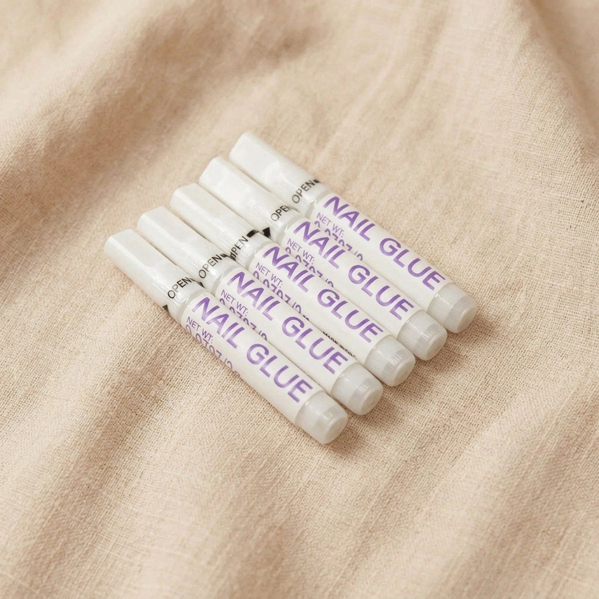 XNails Nail Glue Nagelkleber auf beigem Hintergrund