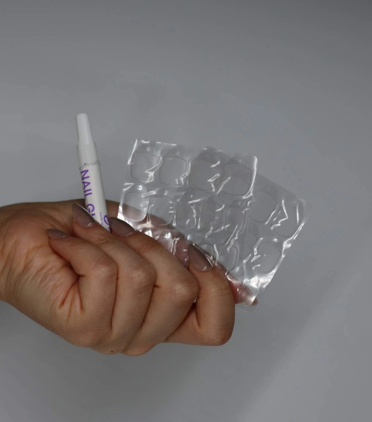Eine Hand hält Nagelkleber und Klebe-Tabs