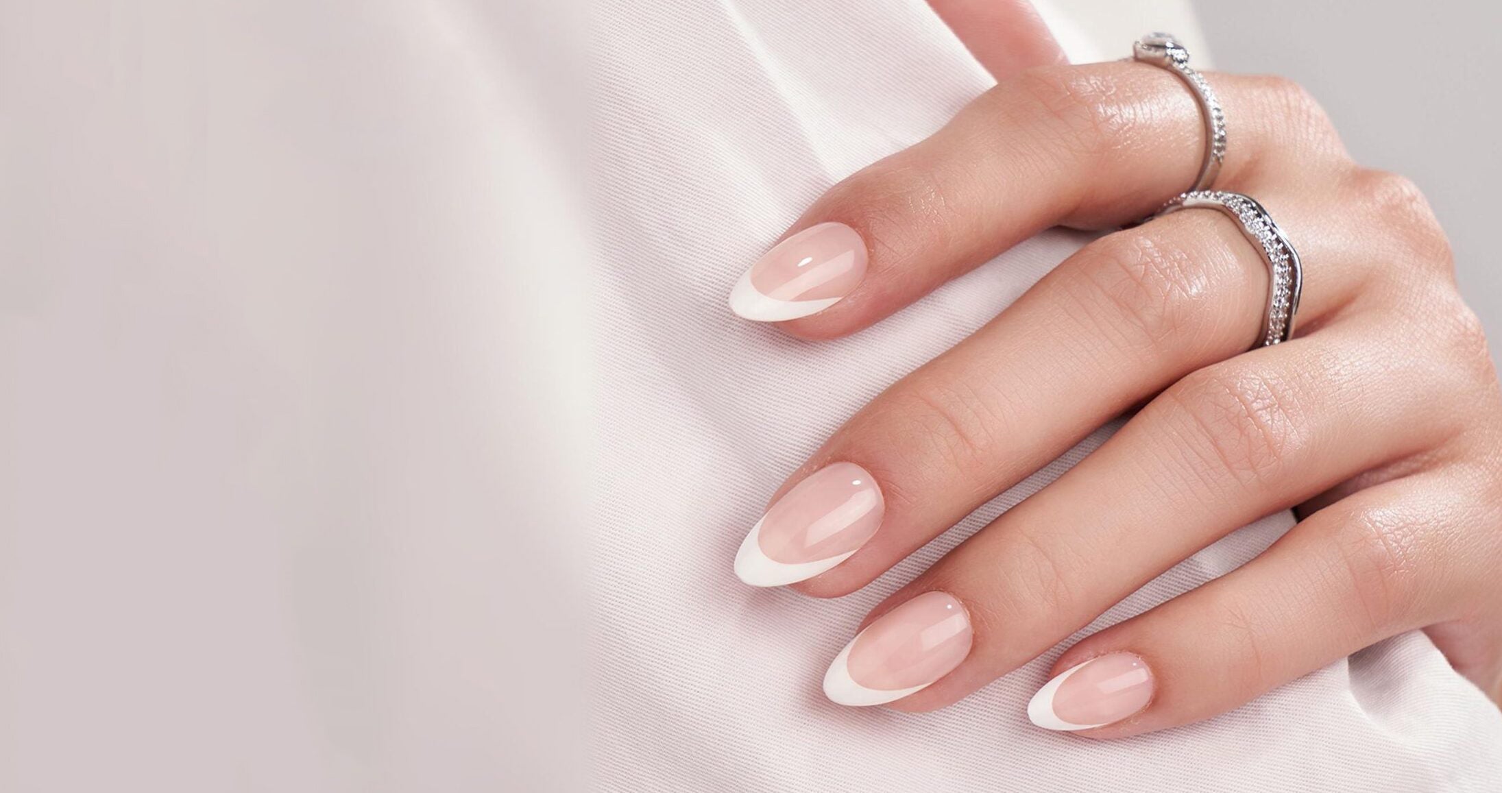 Franska press-on naglar, mandelformade med rosa bas och vita tippar på en hand med ringar