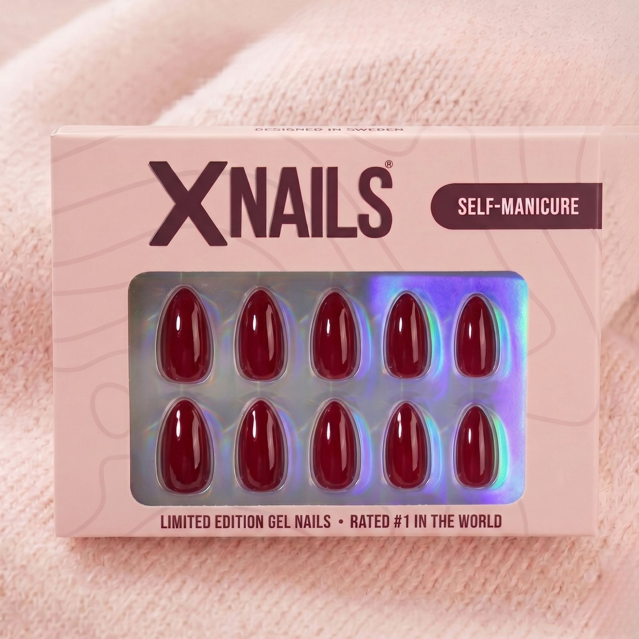 XNails-æske med vinrøde almond press-on negle mod lyserød strikket baggrund