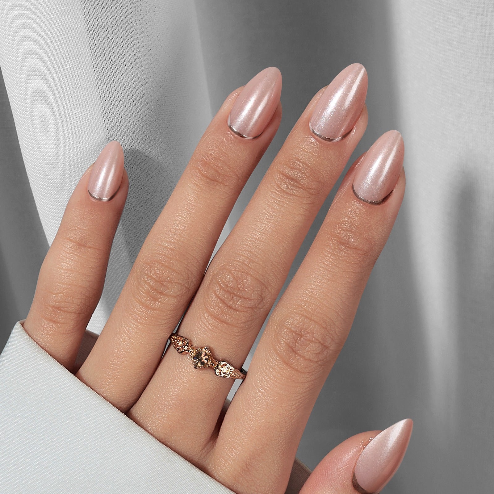 Nude Chrome Press-on-Nägel, mandelförmig mit rosa Schimmer an Hand mit Goldring