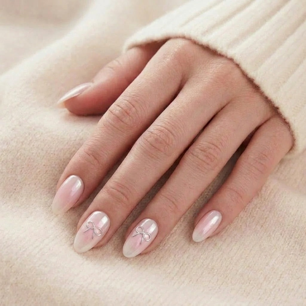 Aura Amoré press-on naglar i pärlemor-chrome med rosa blush-ombre och silverrosett på almond-naglar mot beige stickad tröja