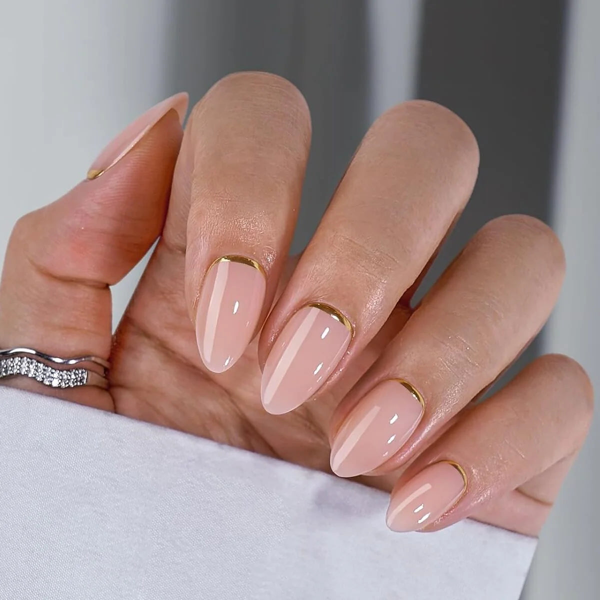 Golden Glimmer Gel-Nägel Nahaufnahme, nudefarbene Mandelform mit Gold-Detail und Silberring