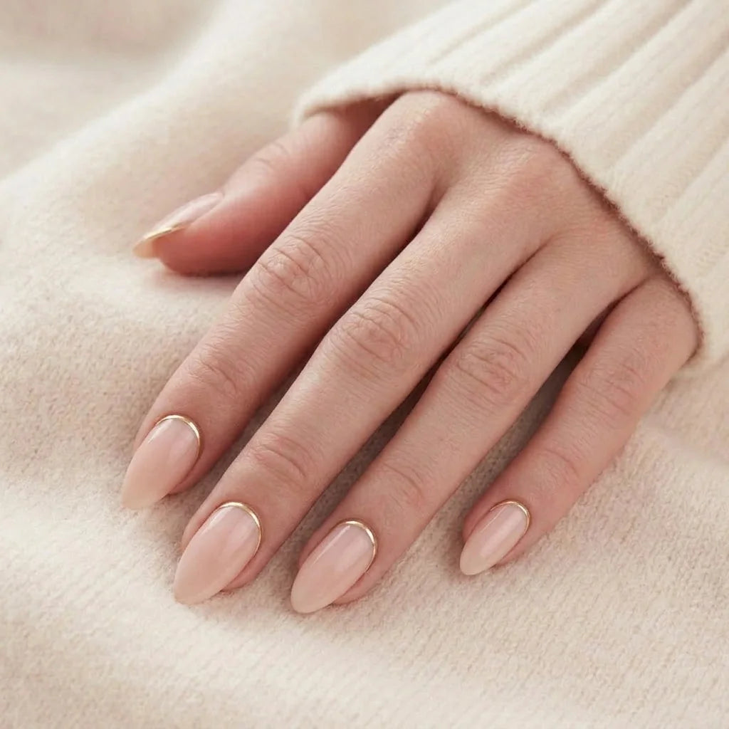 Golden Glimmer negle på hånd peach nude mandel med gulddetalje mod beige strikket trøje