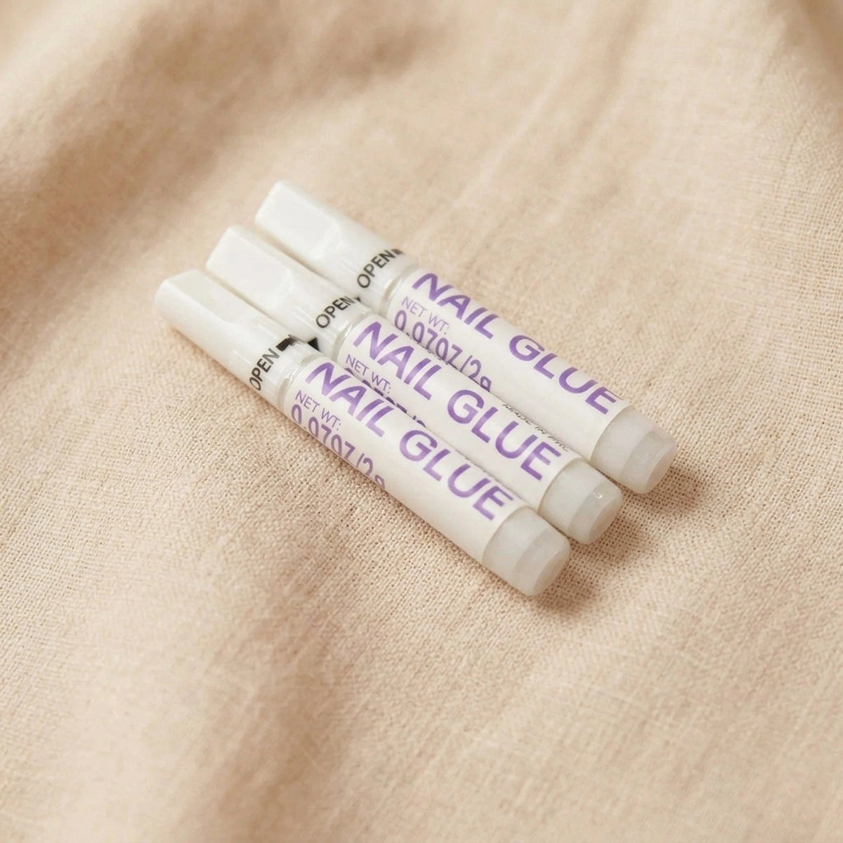 XNails Nail Glue Nagelkleber auf beigem Hintergrund