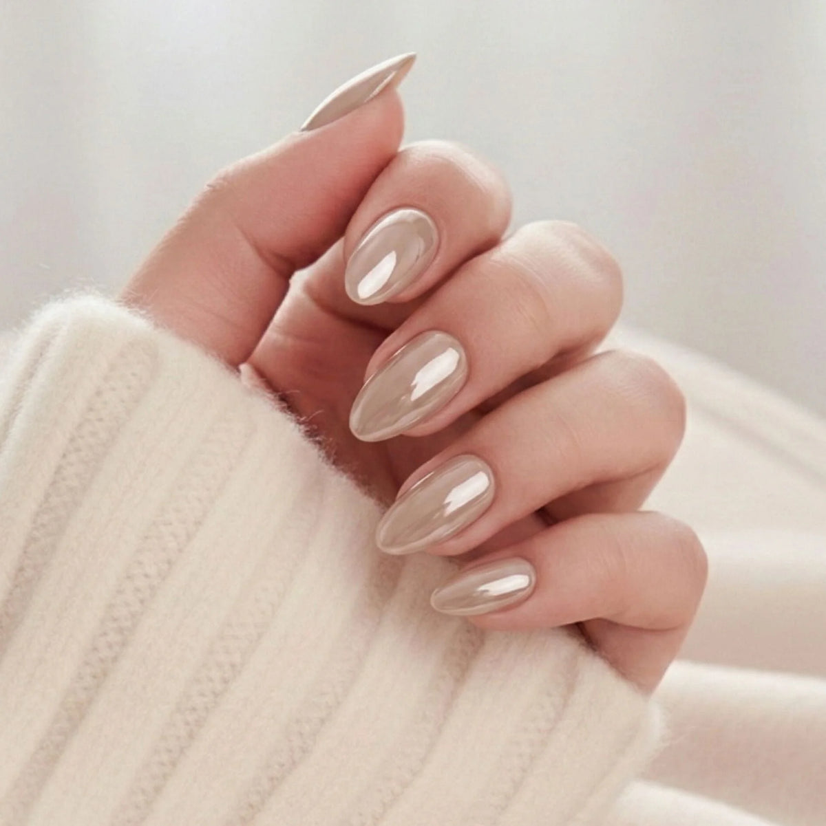 Pearly Perfection press-on negle mandelform i pearl taupe med metallic glans mod cremehvid strikket trøje