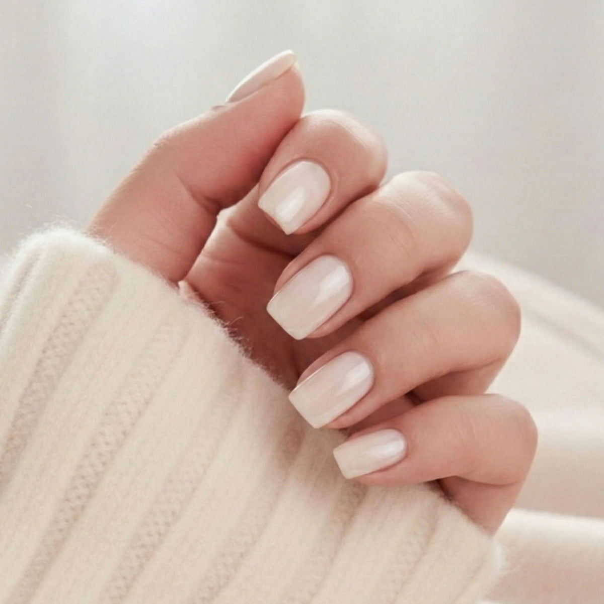 Pure Pearl press-on negle korte square i nude pearl med skimrende glans mod creme strikket trøje