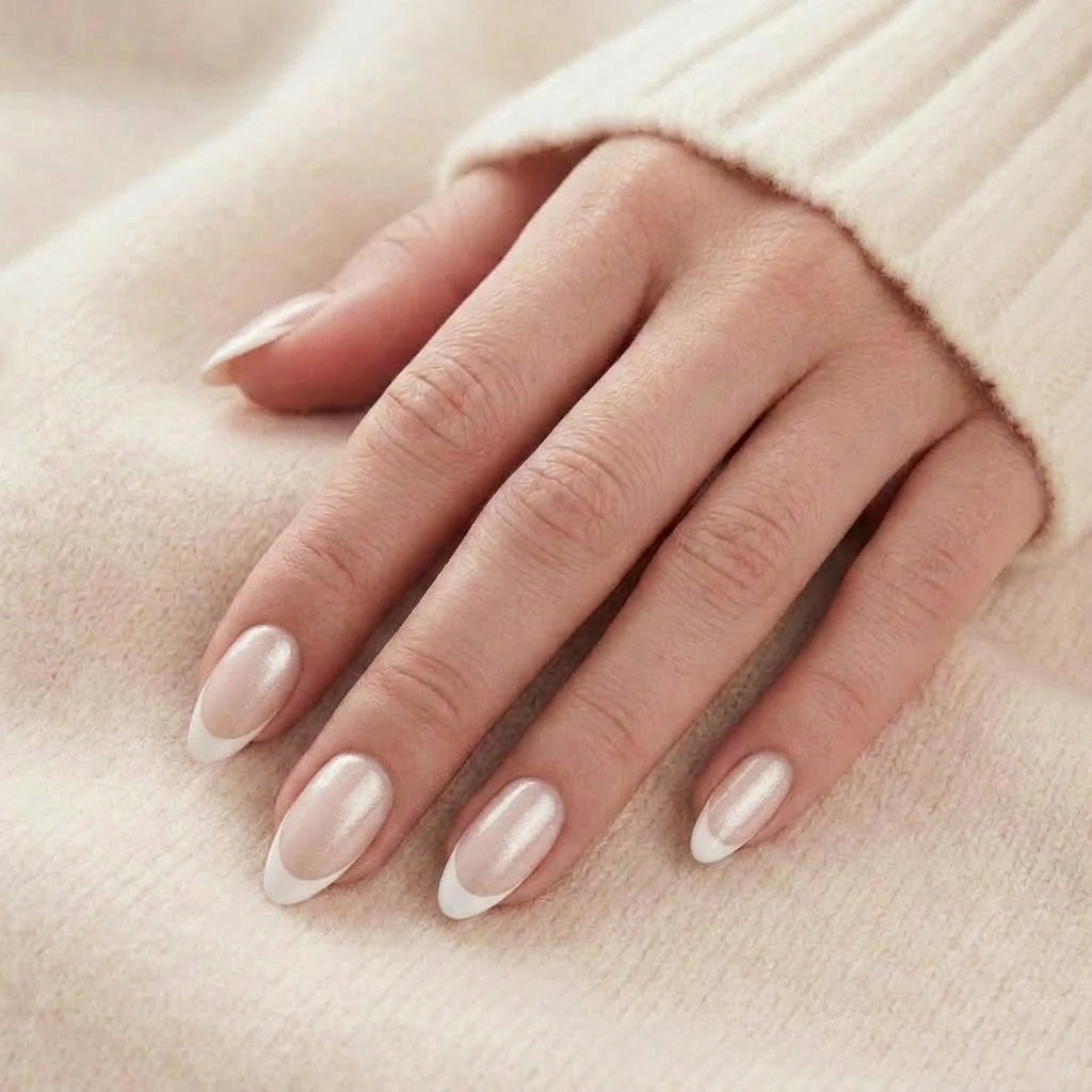 Sweet Sprinkle press-on naglar i mjölkig pärlemor-nude med vit French-tip på hand mot beige stickad tröja