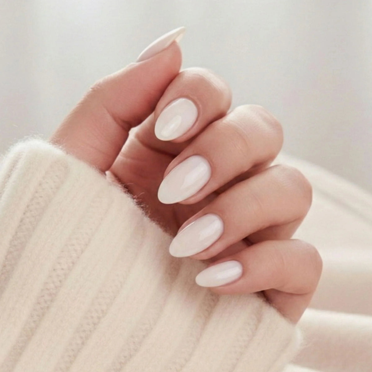 Satin Snow press-on negle, cremehvid mandelmanicure med blød glans mod lys strikket trøje