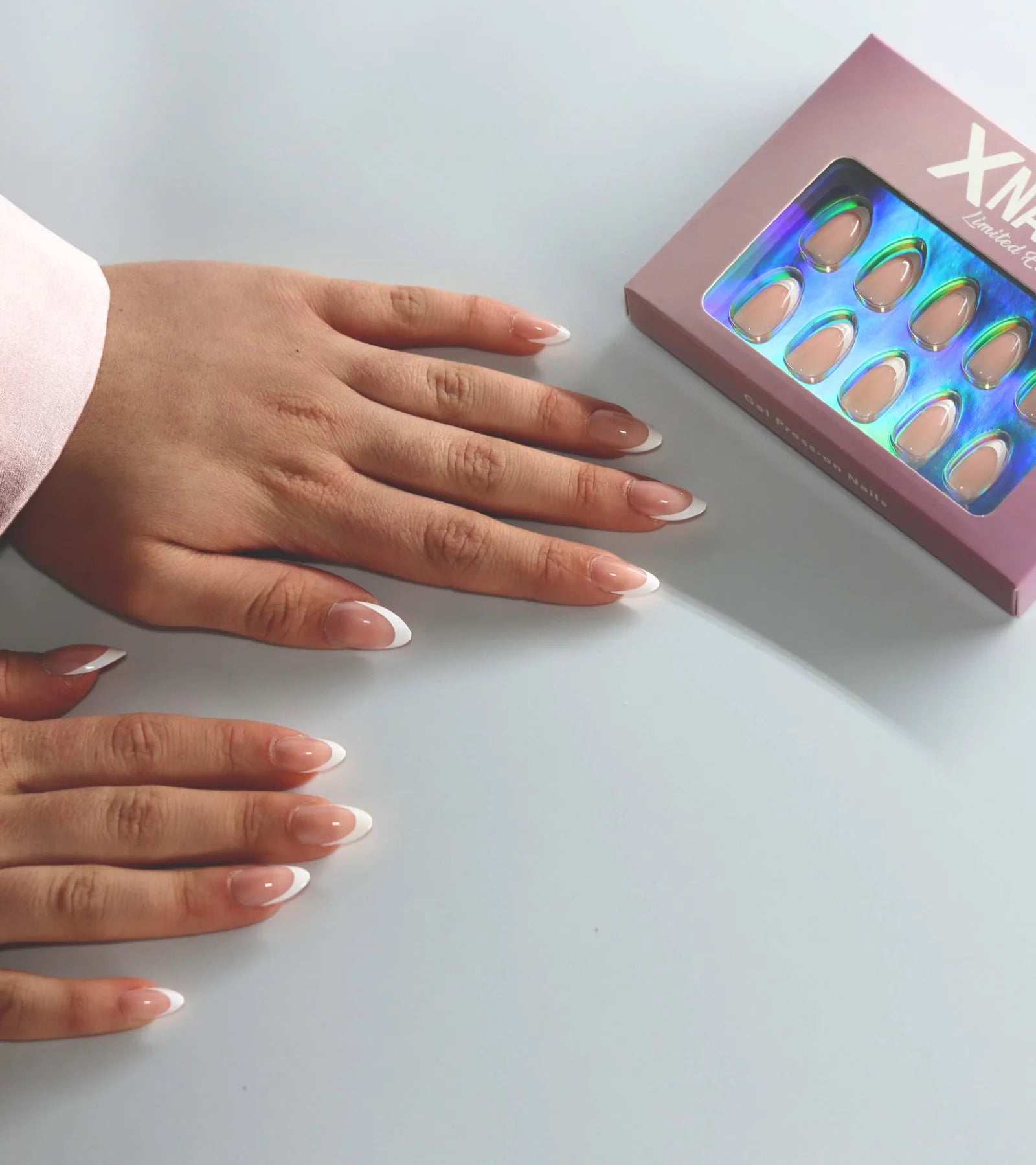 Zwei Hände mit French Press-on Nägeln neben der rosa XNails-Box